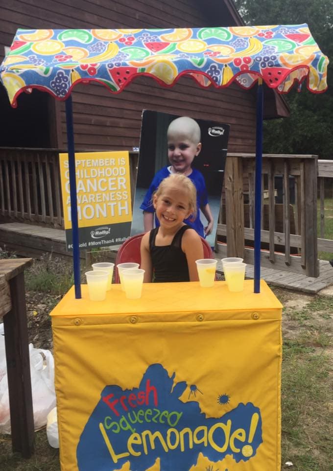 A Cordova Park Elementary School student smiling in front of a lemonade stand to raise money for childhood cancer research